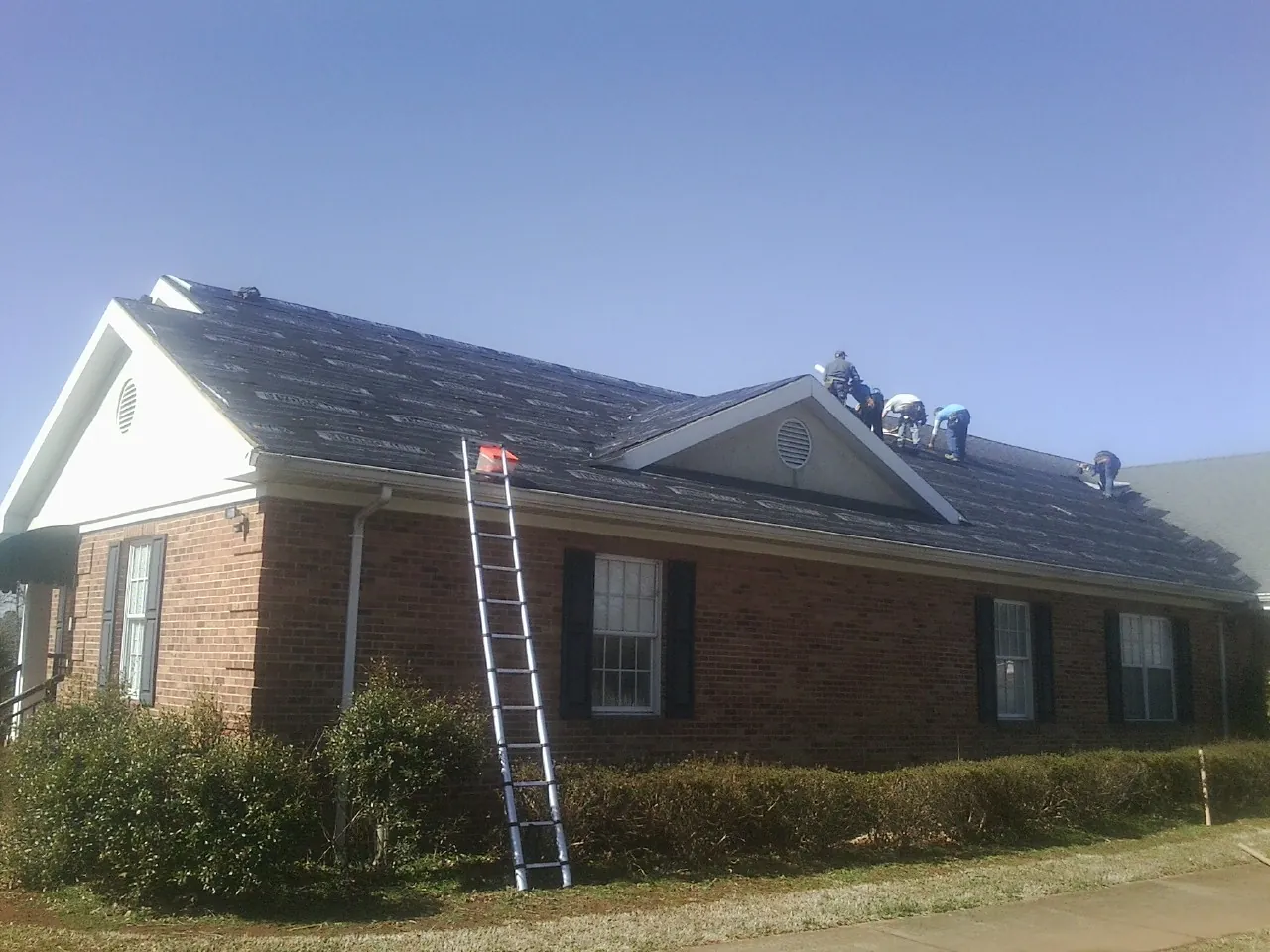 Crew tearing shingles off a brick ranch roof with a ladder set — Metal Roof Repair work by our crew in Boulder