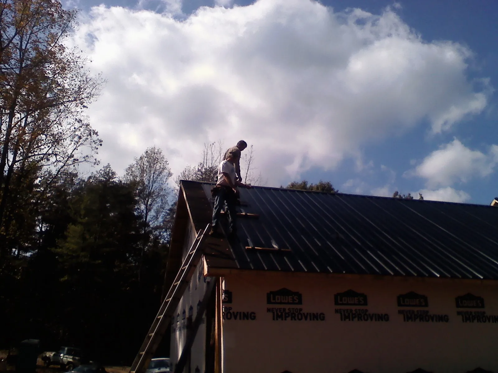 Roofer fastening dark metal panels high against a cloudy sky, from a Roof Inspection job in Boulder